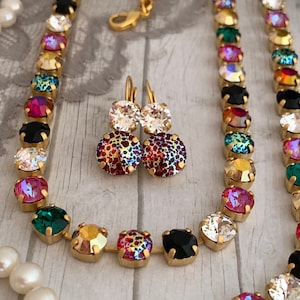 Könnte beinhalten: Eine goldene Kettenkette mit bunten Kristallperlen und passenden Ohrringen. Die Kette hat eine Vielzahl von Farben, darunter Rot, Grün, Blau und Schwarz. Die Ohrringe sind eine kleinere Version der Kette, mit den gleichen Farben und Kristallen.