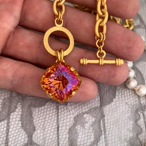 Pode incluir: Um colar de corrente de ouro com um grande pingente de pedra preciosa facetada laranja e rosa. O pingente &eacute; preso a um anel de ouro com um anel de ouro menor na parte superior. O colar tem um fecho de trava de ouro.