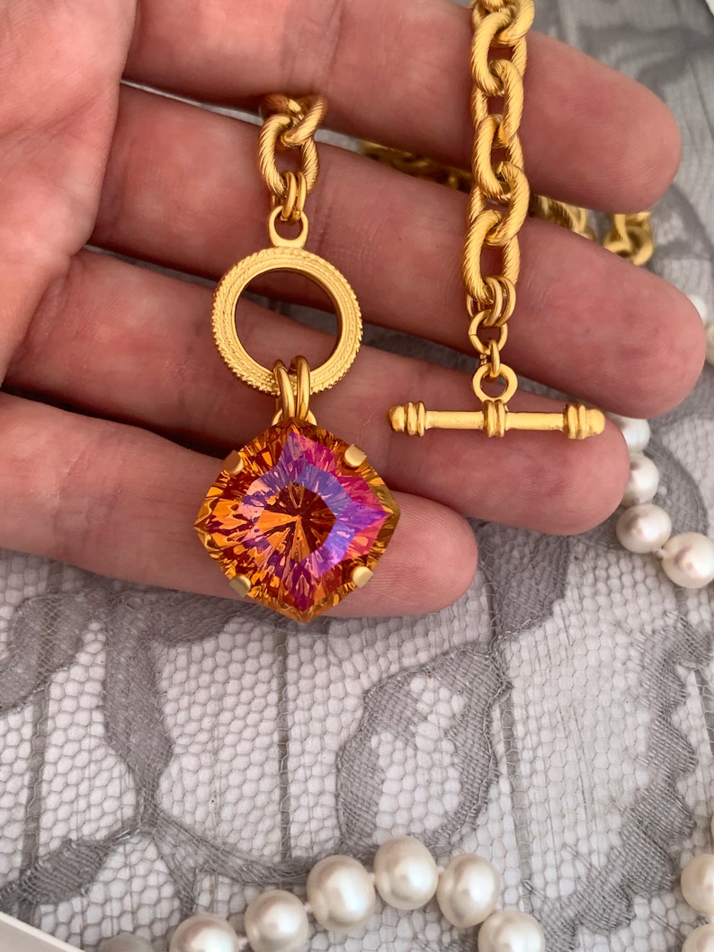 Pode incluir: Um colar de corrente de ouro com um grande pingente de pedra preciosa facetada laranja e rosa. O pingente &eacute; preso a um anel de ouro com um anel de ouro menor na parte superior. O colar tem um fecho de trava de ouro.