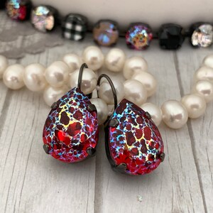 May include: A pair of red teardrop-shaped earrings with a black metal setting. The earrings have a textured, iridescent finish.