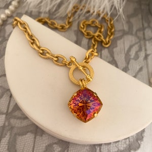 Pode incluir: Um colar de corrente de ouro com fecho de trava e um grande pingente quadrado de pedra preciosa iridescente. A pedra preciosa &eacute; uma mistura de laranja, amarelo e roxo.