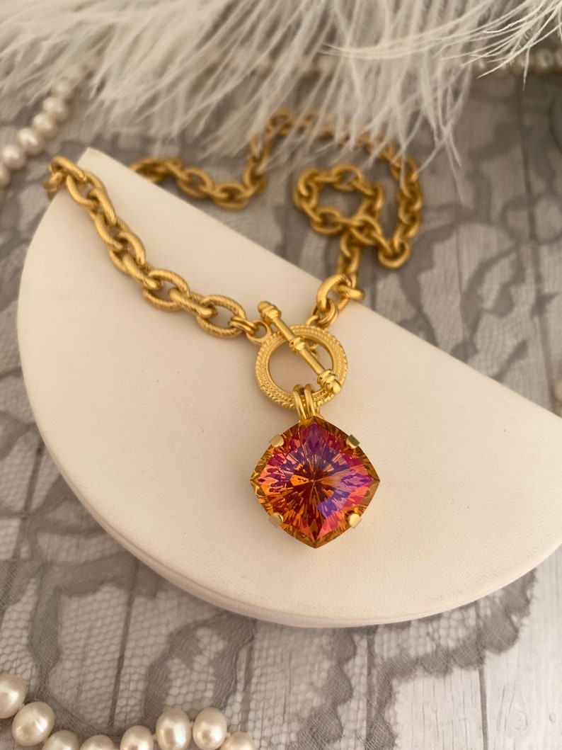 Pode incluir: Um colar de corrente de ouro com fecho de trava e um grande pingente quadrado de pedra preciosa iridescente. A pedra preciosa &eacute; uma mistura de laranja, amarelo e roxo.