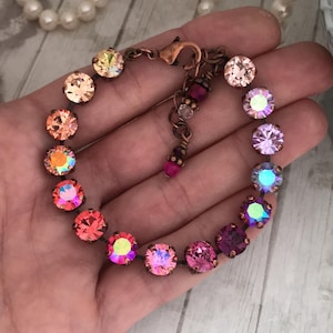 May include: A copper bracelet with a rainbow of iridescent crystals. The crystals are arranged in a gradient from light orange to purple.