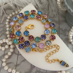 May include: A gold chain necklace with a colorful crystal design. The necklace features a variety of blue, purple, and pink crystals.