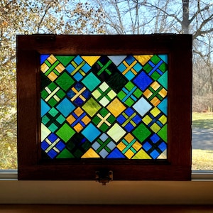 May include: A stained glass window panel with a geometric pattern of green, blue, yellow, and white squares. The panel is framed in dark wood.