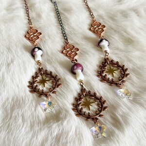 May include: Three mushroom-themed hanging ornaments. The top mushrooms are bronze-colored, with a rainbow-colored mushroom in the center. Each ornament has a chain, a decorative element, a mushroom, a star, a wreath, and a crystal star.
