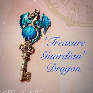 May include: A silver-colored key pendant with a blue dragon design. The dragon has blue wings and is perched above a blue glittery orb. The text on the image reads "Treasure Guardian Dragon" and "High Heorot".