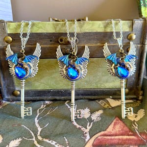 May include: Three silver key necklaces with blue dragon wings and a blue gemstone. The dragon is curled around the key.