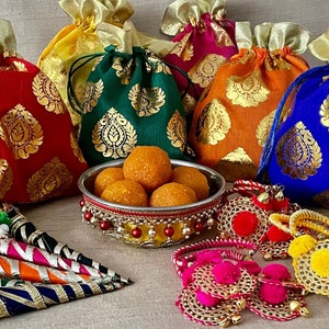 Op de afbeelding: Assortiment van kleurrijke stoffen zakjes met gouden accenten, een kom met ronde oranje snoepjes en decoratieve gouden en roze armbanden met pompoenen.