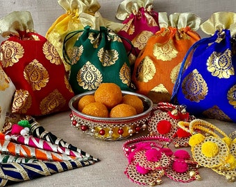 May include: Assortment of colorful fabric pouches with gold accents, a bowl of round orange sweets, and decorative gold and pink bracelets with pom-poms.