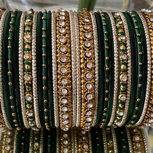 May include: A collection of green and gold bangles. The bangles are decorated with clear gemstones and have alternating bands of dark green, gold, and silver. The gold bands have a floral design.