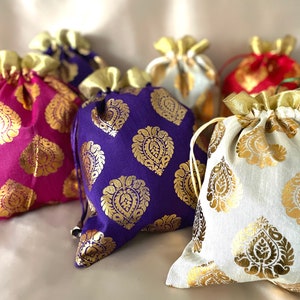 Può includere: Una collezione di sacchetti con coulisse in vari colori, tra cui viola, rosa, rosso e bianco. Ogni sacchetto presenta un motivo paisley dorato e una chiusura con coulisse dorata. I sacchetti sono realizzati in un tessuto lucido.