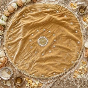 Puede incluir: Un paño circular de terciopelo dorado con un medallón central de cuentas doradas y perlas blancas, rodeado por patrones concéntricos de perlas blancas individuales y un borde con cuentas, sobre un fondo de tela dorada a juego.