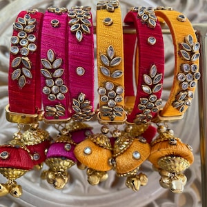 Peut inclure: Une collection de bracelets colorés rouges, roses et jaunes, ornés de décorations en forme de feuilles et de pierres précieuses étincelantes. Les bracelets sont complétés par des breloques en forme de pompons assorties, créant un accessoire vibrant et élégant.