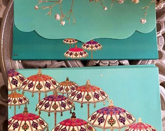 May include: Two rectangular teal envelopes featuring a pattern of ornate, multi-colored parasols with intricate floral and geometric designs. The top envelope has a scalloped flap and the number 1015 printed in the bottom left corner.