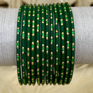 May include: A collection of green bangles with gold and green accents. The bangles are arranged in a vertical stack, showcasing their glossy finish and decorative details. The gold accents are evenly spaced along the surface of each bangle.