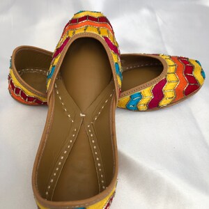 K&ouml;nnte beinhalten: Ein Paar flache Schuhe mit gelber, roter, orangefarbener und blauer Stickerei und spitzer Zehenpartie.