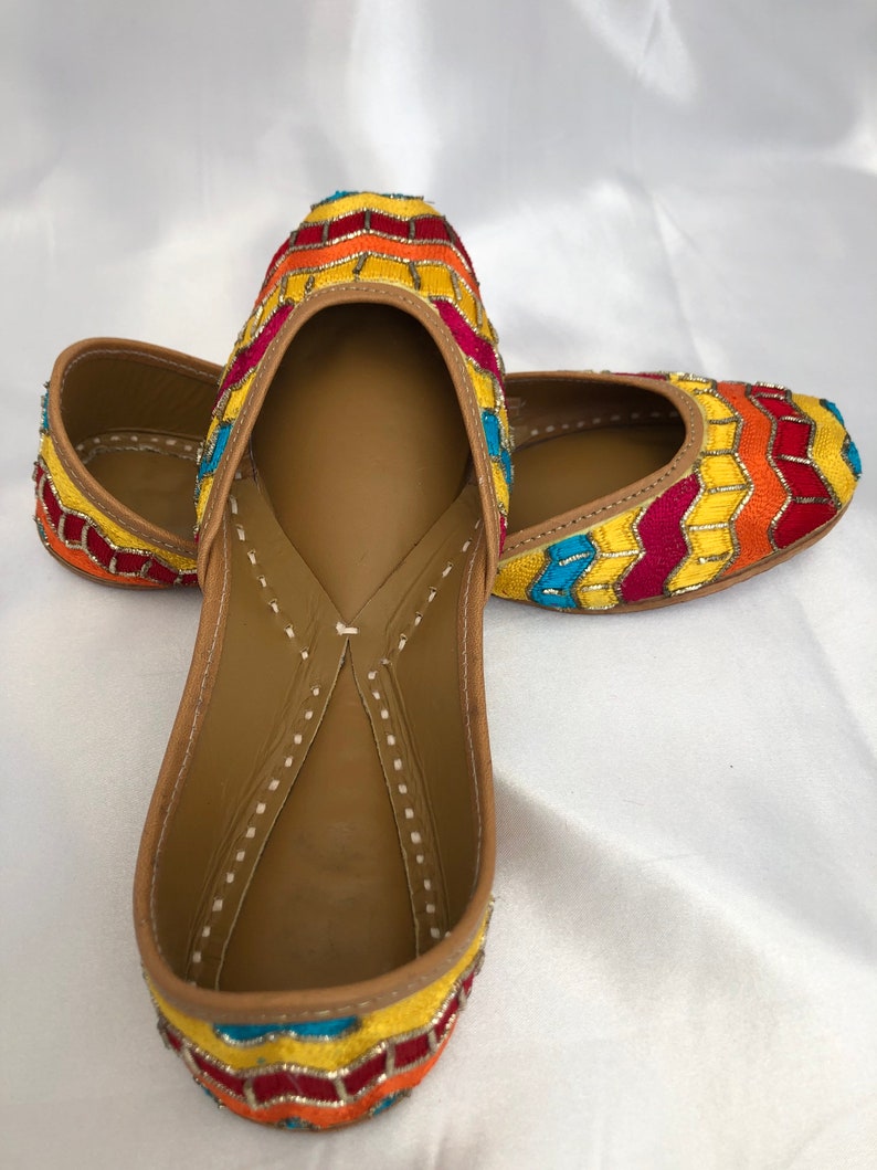 K&ouml;nnte beinhalten: Ein Paar flache Schuhe mit gelber, roter, orangefarbener und blauer Stickerei und spitzer Zehenpartie.