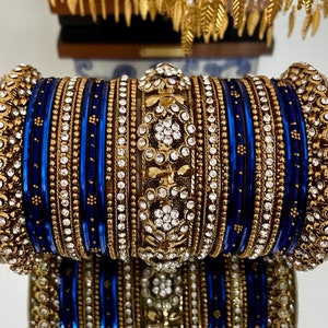 Puede incluir: Un conjunto de brazaletes azules y dorados con pedrería blanca. Los brazaletes están apilados y tienen un diseño decorativo.