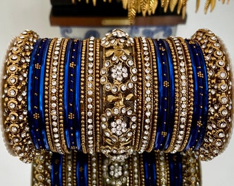 Op de afbeelding: Een set blauwe en gouden armbanden met witte strass steentjes. De armbanden zijn op elkaar gestapeld en hebben een decoratief ontwerp.