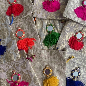 May include: Assortment of small, decorative pouches with gold embroidery and colorful tassels. Each pouch features a round mirror with a gold frame and a tassel in a different color, including pink, red, green, yellow, and blue.