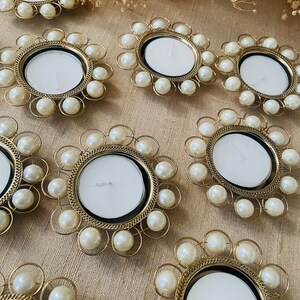 Pode incluir: Conjunto de dez castiçais dourados com detalhes em pérolas brancas. Cada castiçal tem uma parte superior redonda e aberta para uma vela de chá.