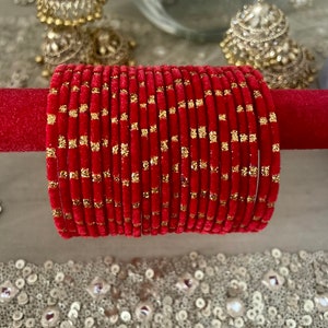 May include: A stack of red velvet bangles with gold glitter accents. The bangles are arranged in a circle and are displayed on a red velvet surface.