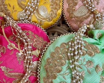 Puede incluir: Cuatro bolsas redondas de tela bordada con cordones y adornos de cuentas de perlas. Las bolsas son de color amarillo, rosa, rojo y verde con bordados dorados de pavos reales.