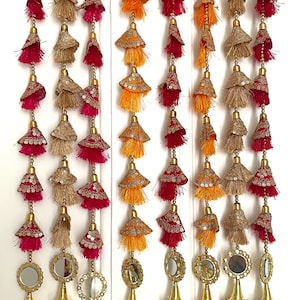 Può includere: Cinque fili di nappe decorative con accenti dorati e specchi in fondo. Ogni filo presenta un mix di nappe in tessuto rosso, arancione e oro.