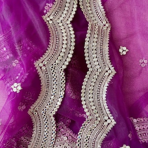 Może przedstawiać: Zbliżenie na żywy fioletowy materiał z misternymi srebrnymi i przezroczystymi zdobieniami. Wzór ma falisty brzeg z rzędami małych, okrągłych akcentów i większych, odblaskowych detali.