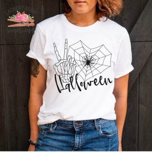 May include: White t-shirt featuring a black skeleton hand making a peace sign, a spider web with a spider in the centre, and the word "Halloween" written in a script font.