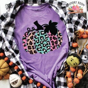 Op de afbeelding: Paars T-shirt met een afbeelding van een veelkleurige luipaardprint pompoen. De pompoen is roze, bruin, turquoise en zwart.