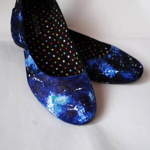 K&ouml;nnte beinhalten: Ein Paar blaue Canvas-Ballerinas mit Galaxie-Druck. Die Innenseite der Schuhe hat einen schwarzen Hintergrund mit bunten Punkten.