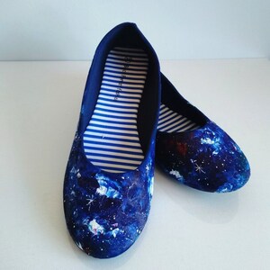 K&ouml;nnte beinhalten: Ein Paar blaue Ballerinas aus Canvas mit einem Galaxie-Druck. Das Innere der Schuhe hat wei&szlig;e und blaue Streifen und der Text "Back to Basics" ist auf der Innenseite des linken Schuhs aufgedruckt.