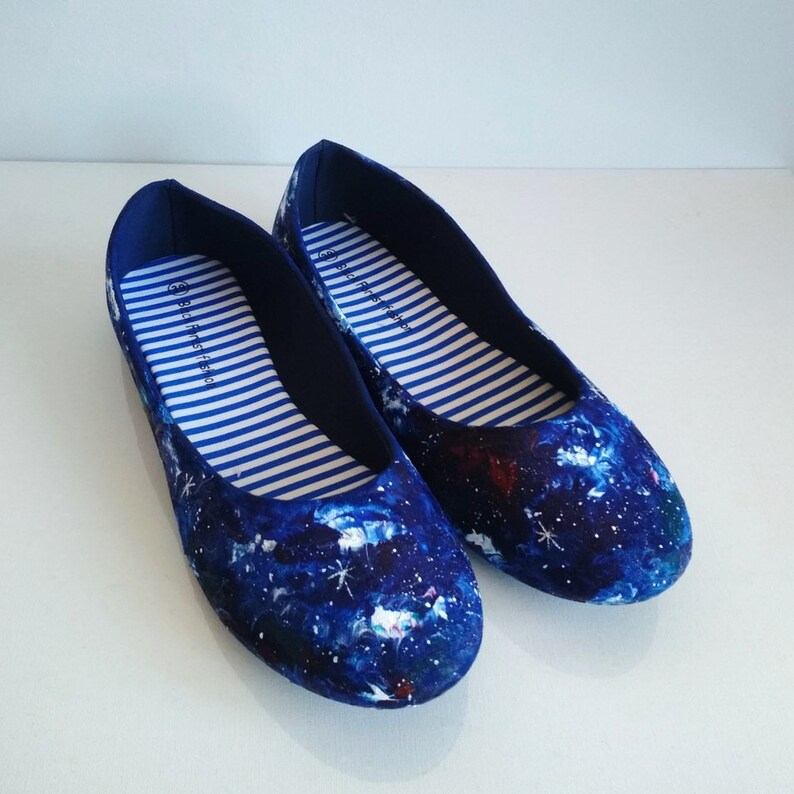K&ouml;nnte beinhalten: Ein Paar blaue Canvas-Ballerinas mit Galaxie-Druck. Die Schuhe haben wei&szlig;e Streifen innen und der Text "first & free" ist auf der Innenseite jedes Schuhs aufgedruckt.