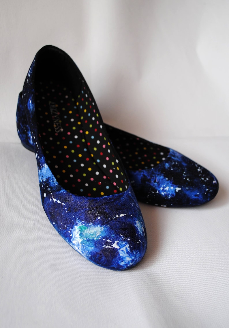 K&ouml;nnte beinhalten: Ein Paar blaue Canvas-Ballerinas mit Galaxie-Druck. Die Innenseite der Schuhe hat einen schwarzen Hintergrund mit bunten Punkten.