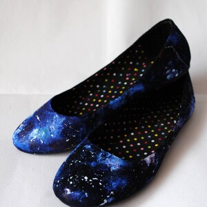 K&ouml;nnte beinhalten: Ein Paar blaue Ballerinas mit Galaxie-Druck. Die Ballerinas haben ein schwarzes und wei&szlig;es Punktefutter.
