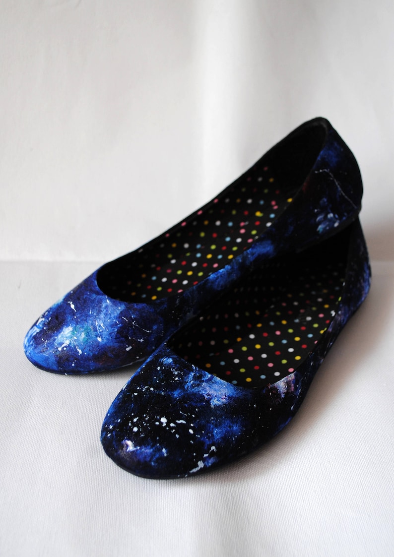 K&ouml;nnte beinhalten: Ein Paar blaue Ballerinas mit Galaxie-Druck. Die Ballerinas haben ein schwarzes und wei&szlig;es Punktefutter.
