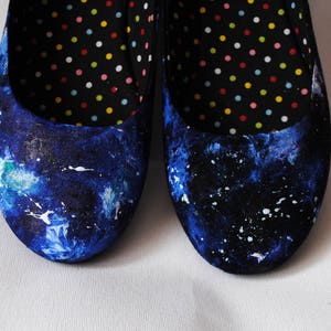 K&ouml;nnte beinhalten: Ein Paar blaue Ballerinas aus Canvas mit einem wei&szlig;en Spr&uuml;hfarbendesign. Die Ballerinas haben ein schwarzes und wei&szlig;es Punktefutter.