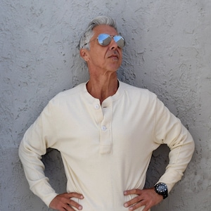 May include: A man wearing a white long-sleeved shirt with a button placket, black pants, and a black wristwatch. He is wearing mirrored sunglasses and looking up.