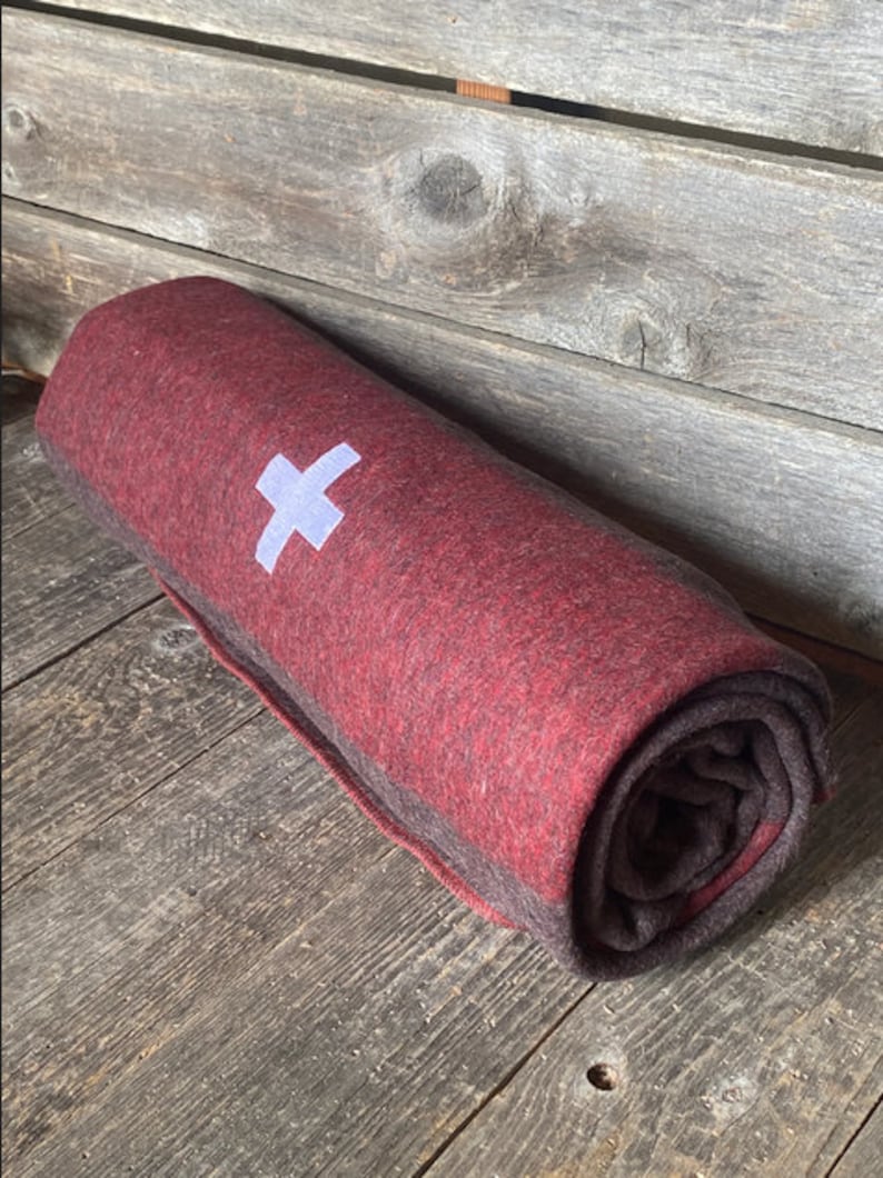 May include: A rolled up red and brown wool blanket with a white cross embroidered on it.
