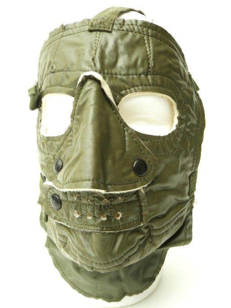 K&ouml;nnte beinhalten: Eine gr&uuml;ne Milit&auml;r-Gesichtsmaske mit gepolstertem Nasen- und Kinnbereich. Die Maske hat eine Klappe, die Mund und Kinn bedeckt, und ein Band, das um den Kopf geht.