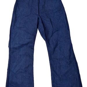 May include: Dark blue denim pants with two large front pockets. The pants have a high waist and a wide leg, with a button and zipper closure. The fabric appears to be a medium weight denim.