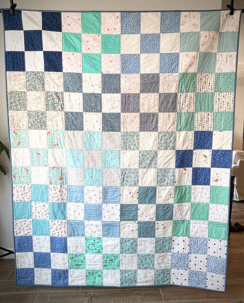 K&ouml;nnte beinhalten: Eine Patchwork-Decke mit einem Schachbrettmuster in Blaut&ouml;nen, Gr&uuml;n und Wei&szlig;. Die Decke besteht aus vielen verschiedenen Stoffquadraten, jedes mit einem einzigartigen Muster.