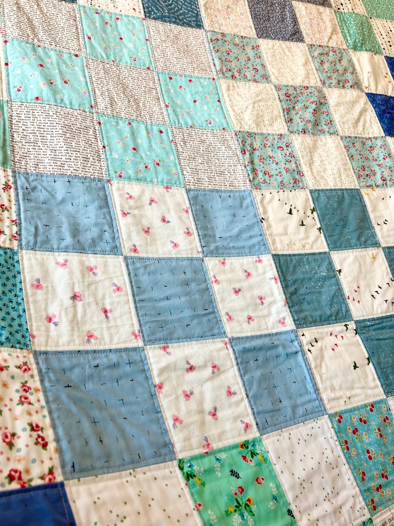 K&ouml;nnte beinhalten: Eine Patchwork-Decke mit einem karierten Muster in Blaut&ouml;nen, Wei&szlig; und Gr&uuml;n. Die Decke besteht aus verschiedenen Stoffen mit unterschiedlichen Mustern, darunter Blumenmuster, Punkte und einfarbige Stoffe.
