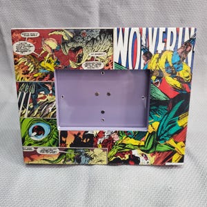May include: Rectangular picture frame featuring comic book panels with the word "WOLVERINE" in large letters. The frame has a purple interior and is decorated with colorful illustrations of action scenes.