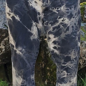May include: Dark wash denim jeans with a unique bleach dye pattern. The jeans have a high-waisted fit and a straight leg. The bleach dye creates a marbled effect in shades of white and gray, giving the jeans a distinctive look. The jeans are a classic five-pocket style.