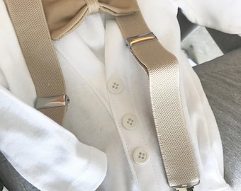 Puede incluir: Un body blanco con una pajarita beige y tirantes a juego. Los tirantes tienen clips metálicos plateados. El body tiene botones blancos. Este conjunto es perfecto para un bebé o un niño pequeño.