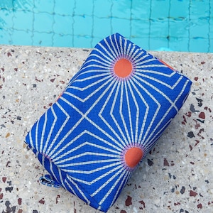 Puede incluir: Una bolsa de aseo de patrón geométrico azul y blanco con acentos naranja y rosa. La bolsa está sobre una superficie texturizada.