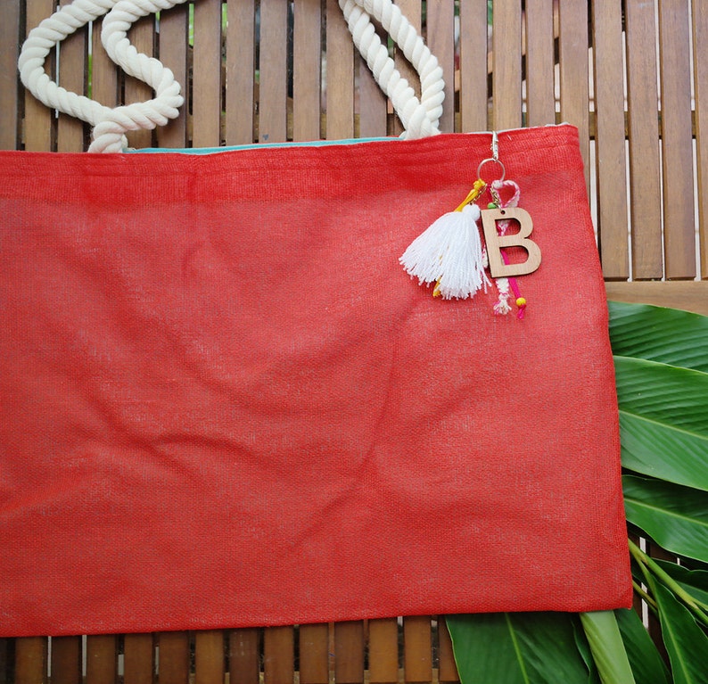 May include: A red tote bag with white rope handles and a wooden letter "B" charm with colourful tassels hanging from it.